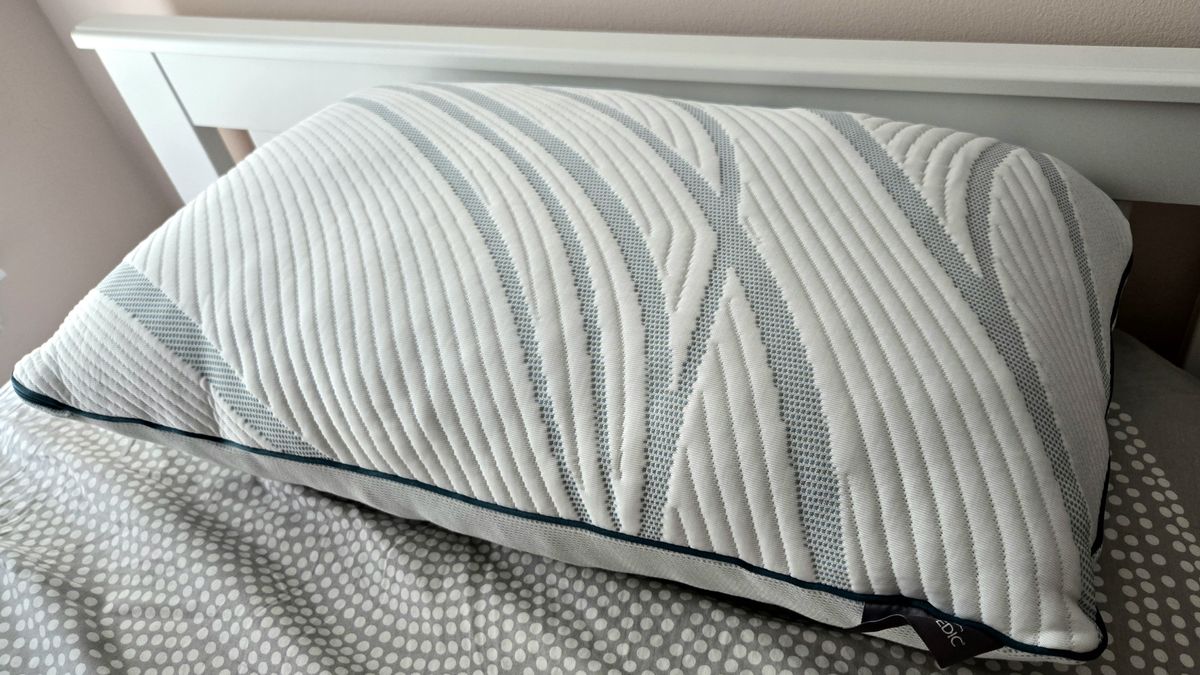 The front side of the Tempur-Pedic Tempur-Adapt ProAdjust Pillow, featuring Tempur's signature blue and white striped design, on top of a bed with a grey and white comforter