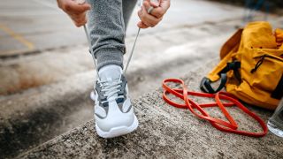 Man tying shoe on concrete step next to resistance band and yellow bag