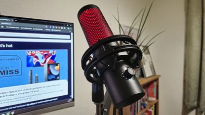 The HyperX Quadcast 2 in Hamish Hector's office on a mic arm in front of a PC screen and a bookshelf