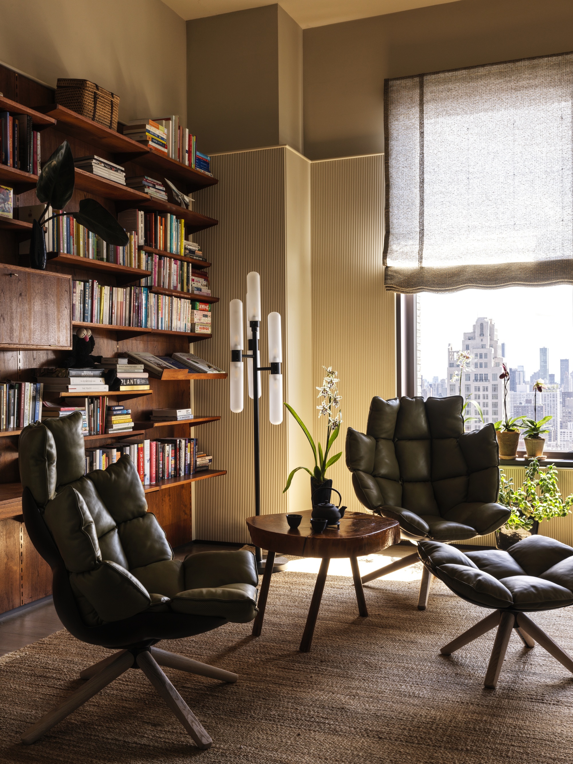 home office with wall of bookshelves, fluted wall detail, linen roman shades, jute rug, two leather armchairs and timber side table and ottoman