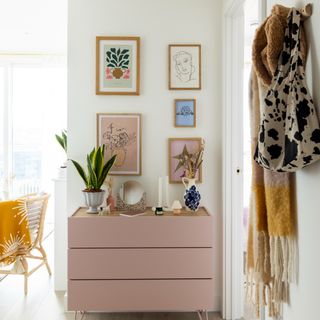 White painted hallway with pink dresser decorated with decorative items and artwork hanging