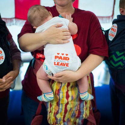 A woman holds a baby with a sticker promoting paid leave on their bottom