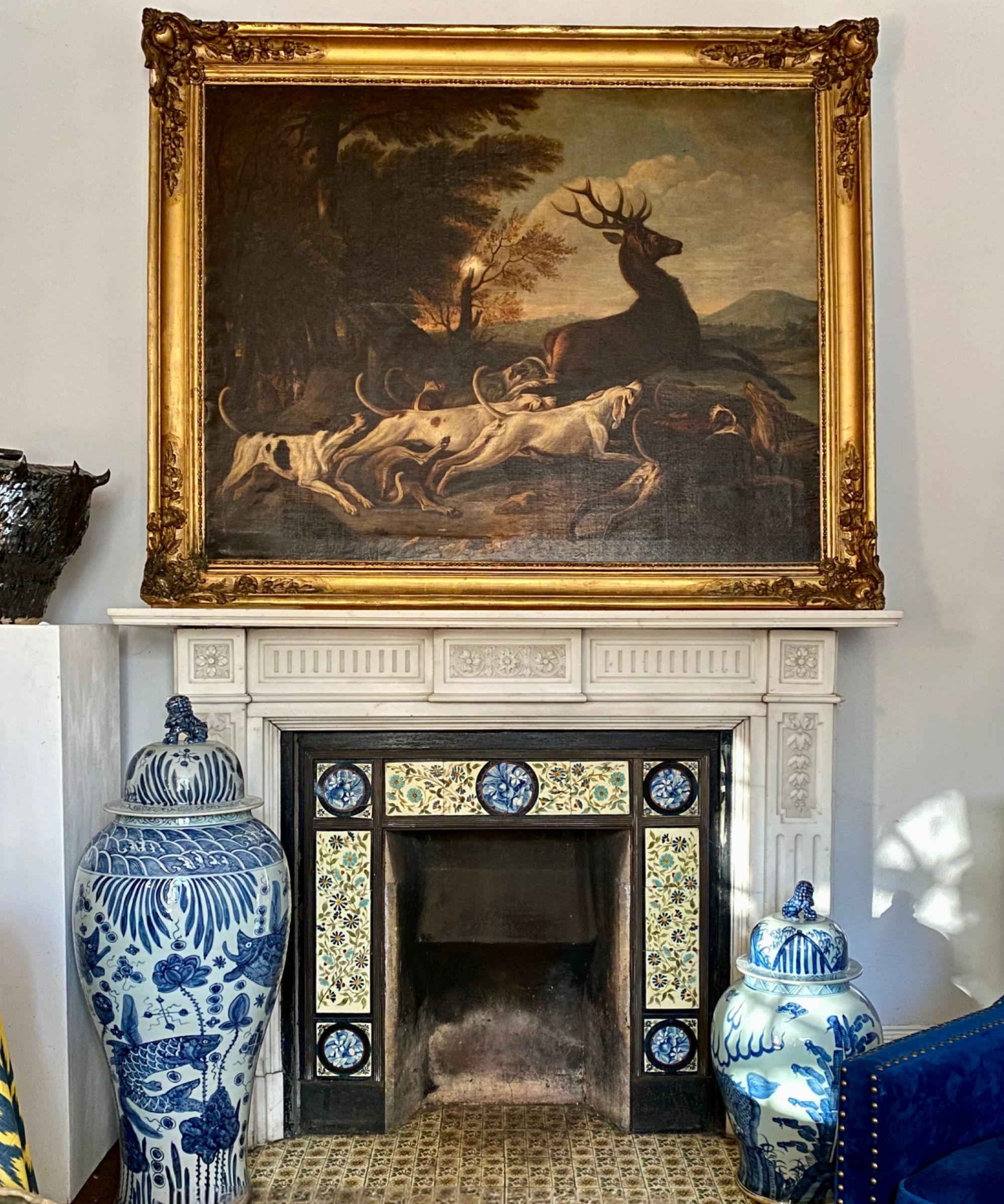 Fireplace with tiling, blue and white antique ginger jars, and an antique oil painting on the mantel of a stag and dogs.