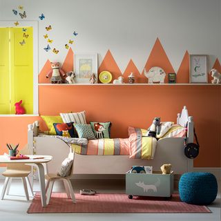 girls nursery with orange painted wall scape and cot bed