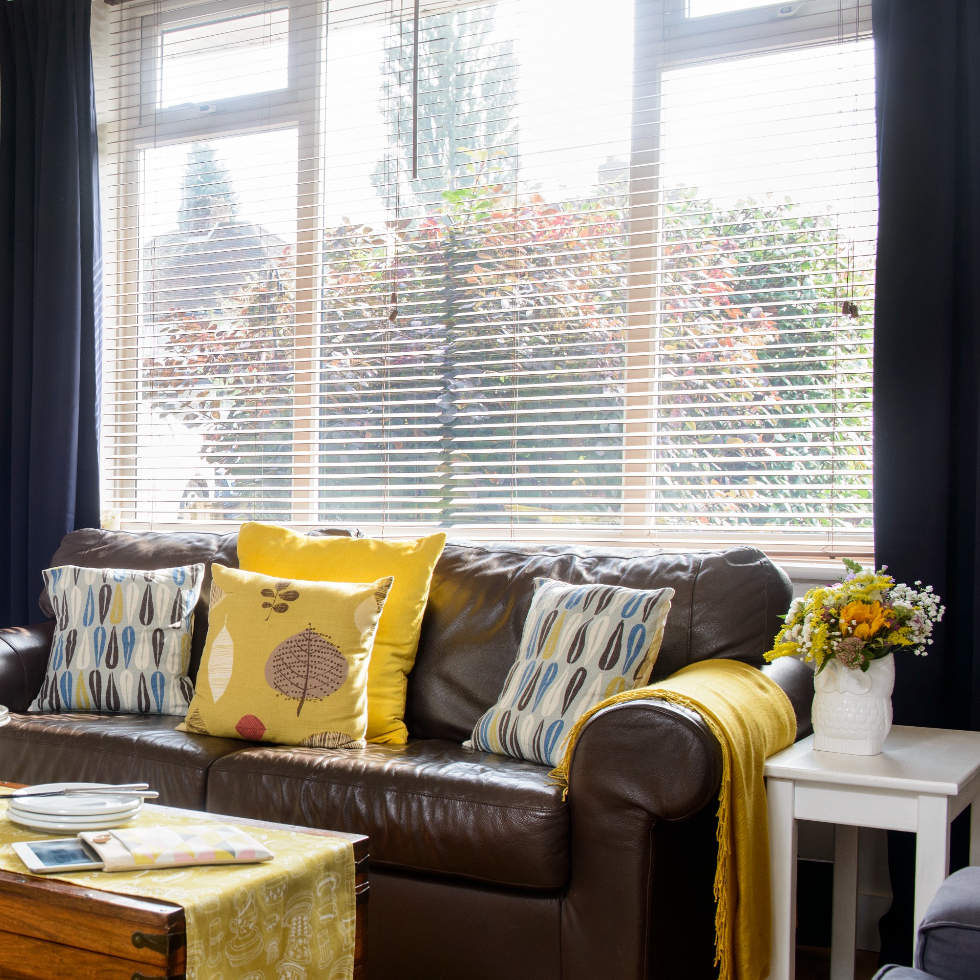 A conservatory living room with a brown leather sofa and Venetian blinds covering the window