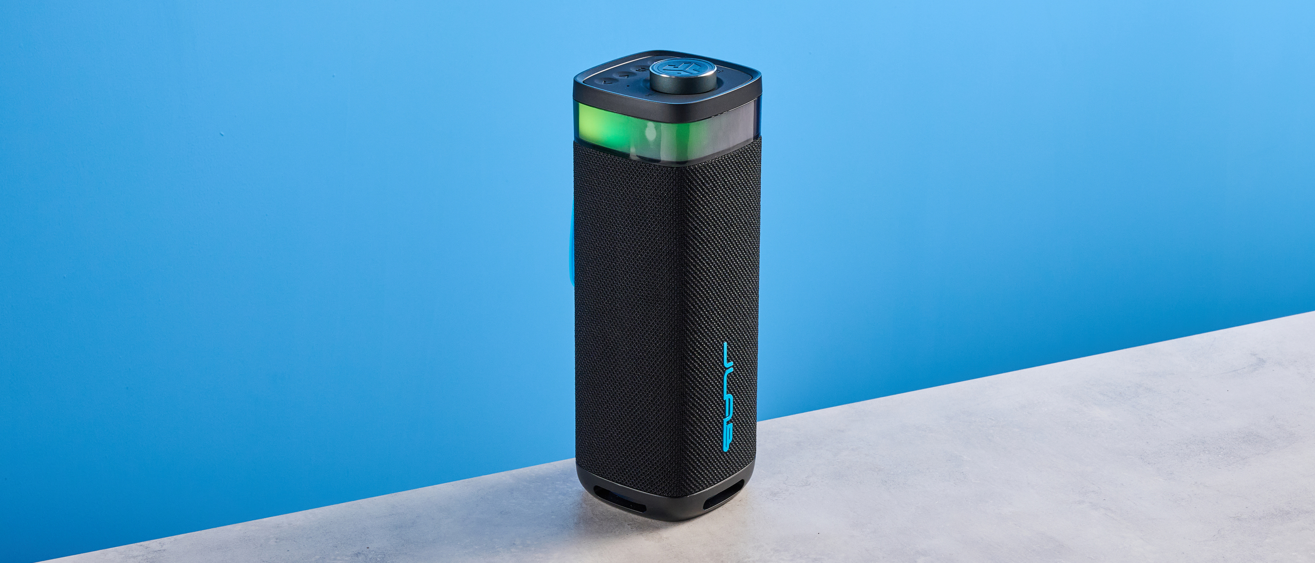 the jlab jbuds party speaker with LED rainbow lights photographed against a blue background