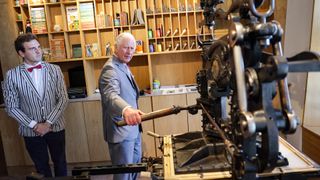 With the assistance of Artist, Aidan Saunders, Prince Charles, Prince of Wales creates a lino print on an 1800's printing press during a visit to Hay Castle
