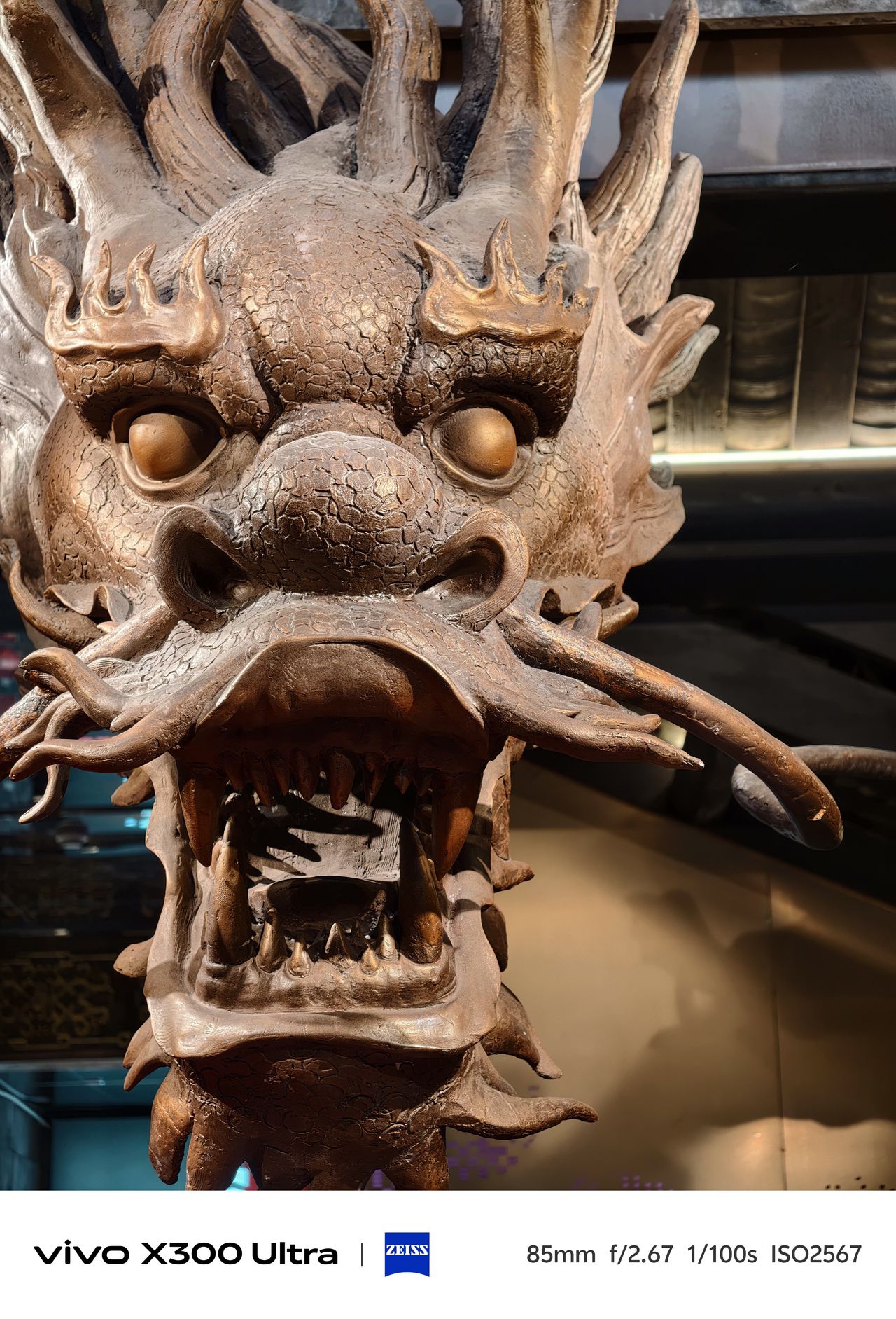A detailed macro shot of a metallic, golden-brown sculpted dragon head with an open mouth.