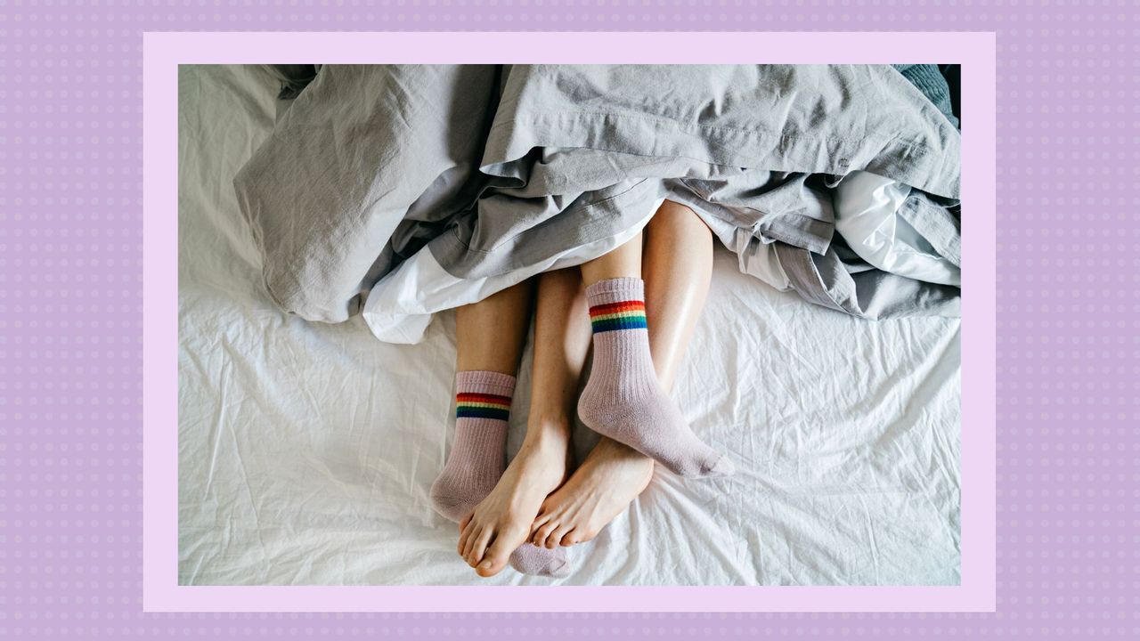 High angle view of two women&#039;s feet lying in bed together. Couple wearing socks to bed. One woman is wearing rainbow flag&#039;s socks. They are sleeping together.