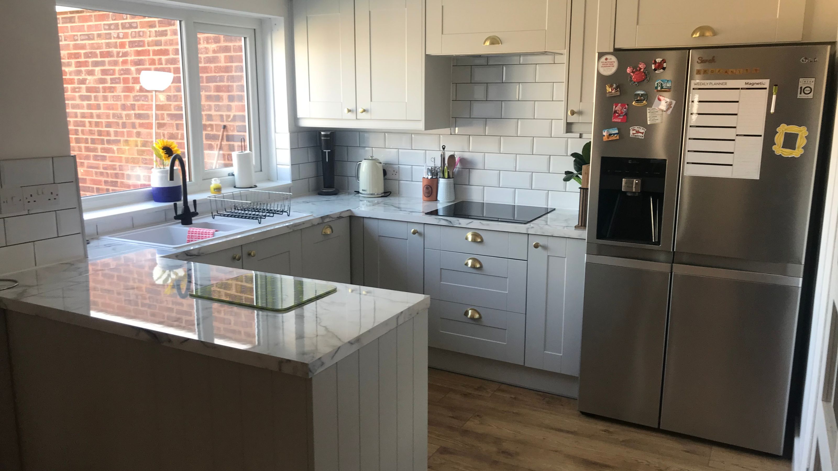 Kitchen with light grey cupboards, marble look worktops, white metro tiles, a peninsula and American-style fridge freezer
