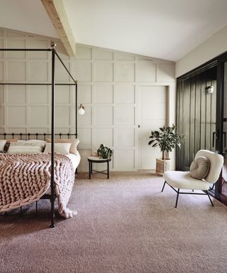 A large bedroom with a four-poster bed and pink carpet with beige wall paneling decor