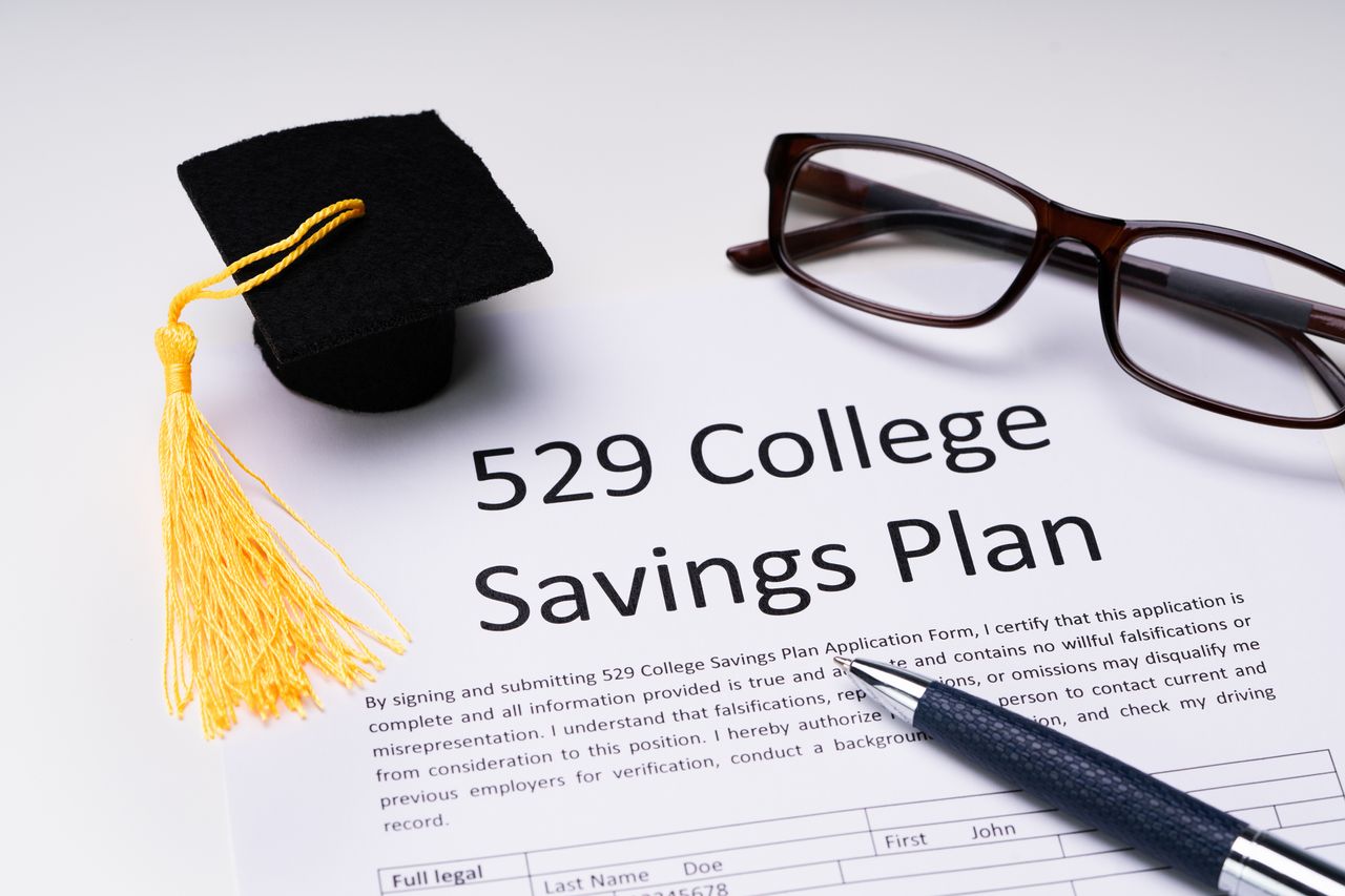 529 plan form with small graduation hat, spectacles and pen over white background.