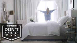 Memorial Day mattress sales: A person holding curtains open and looking out of the window, with a Saatva Classic bed in the foreground and a badge saying 'DON'T MISS'