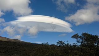 a saucer-shaped cloud above a mountain in a blue sky