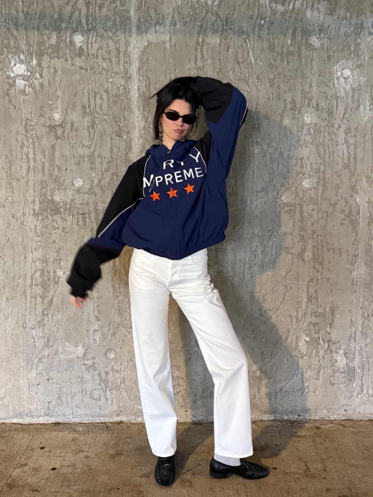 Kendall Jenner wearing a Marty Supreme navy blue windbreaker with white jeans and black loafers.