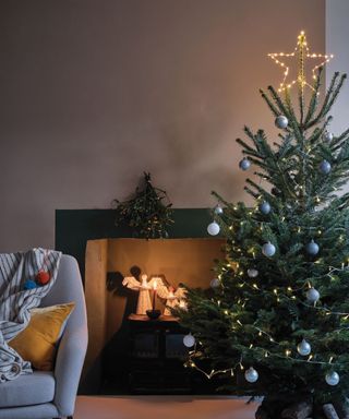 A simple christmas tree with blue baubles and star topper by a fire