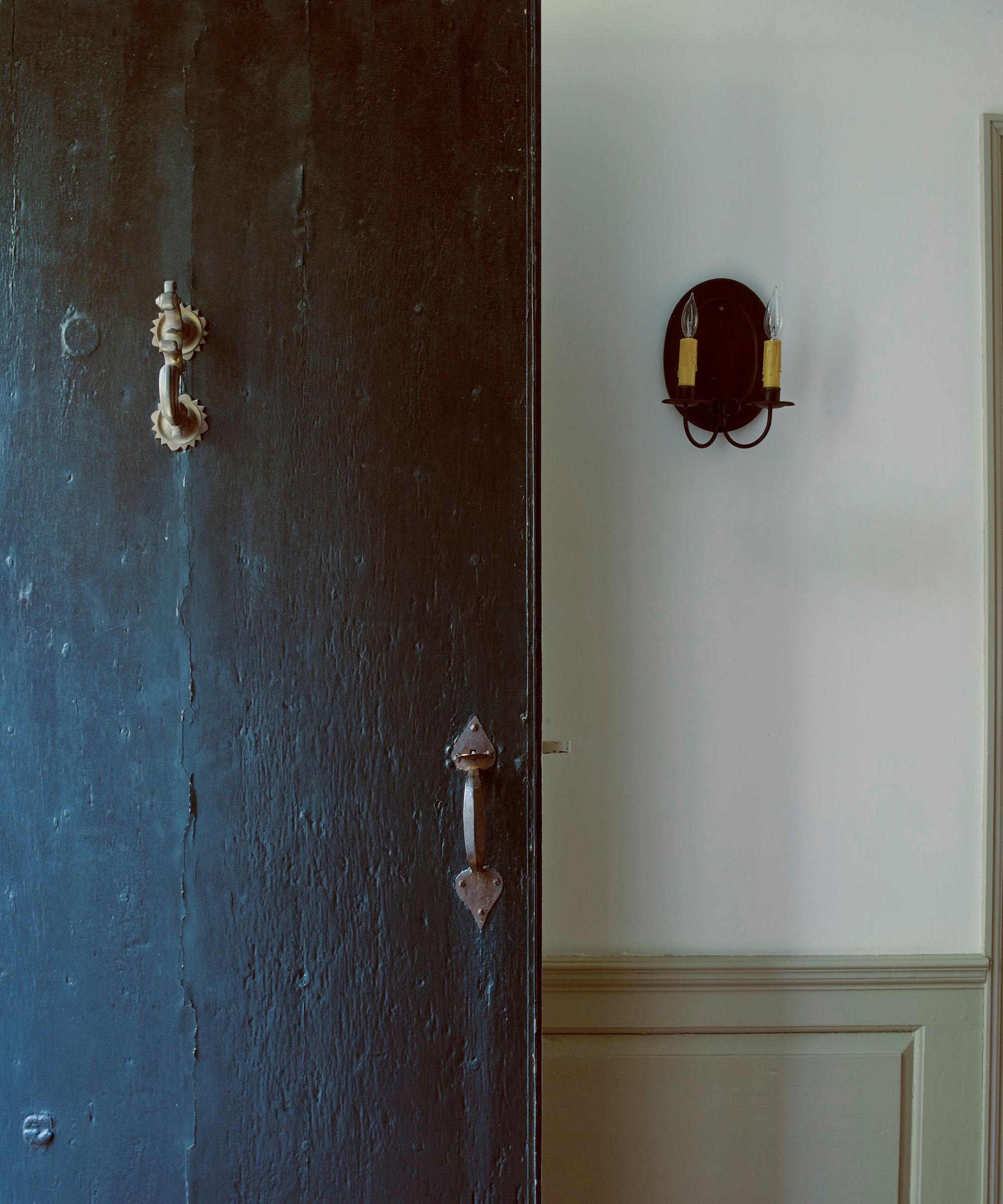 An open dark blue front door with gold knocker and white panelled walls.