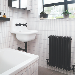 black raditor in white bathroom. White tiled bath, white tiled walls and white sink The sink has black taps and piping.