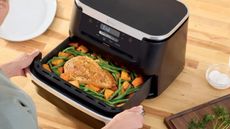 Ninja Foodi Flexbasket air fryer on a wooden countertop with the drawer full of chicken and vegetables