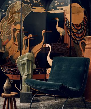 A dark blue velvet chair in front of an artistic painted room divider
