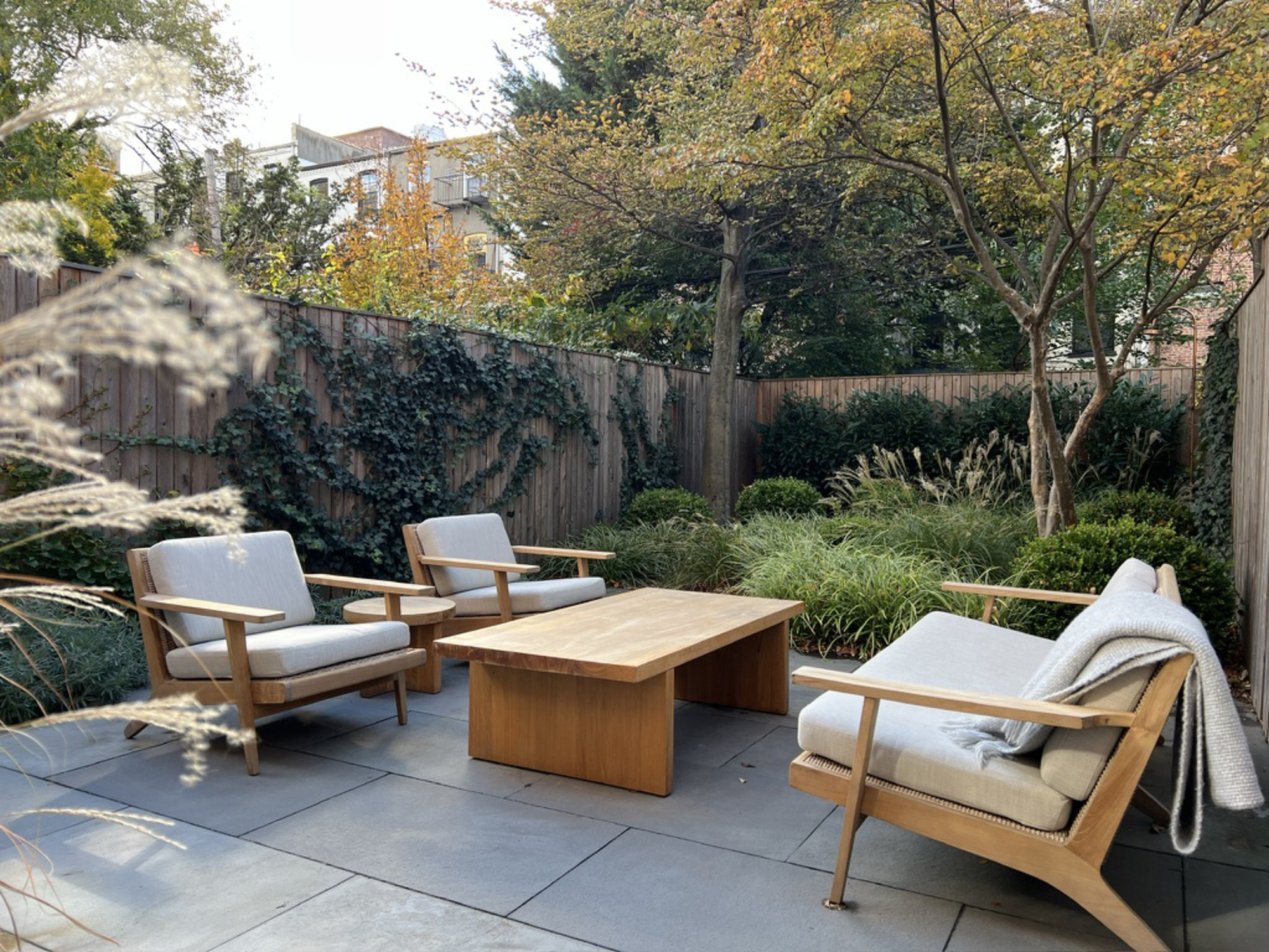 A patio with a fence, ornamental grasses, and a seating area with modern furniture