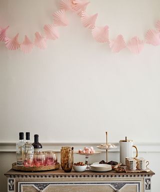 Metallic drinks trolley decorated with glassware, drinks, snacks, white painted walls, pink paper wall decoration
