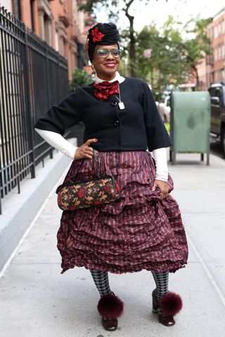 Arlinda McIntosh in an over 60 outfit featuring a white top, black sweater, red striped skirt, black and white tights, black shoes with a red puff ball, and printed purse.