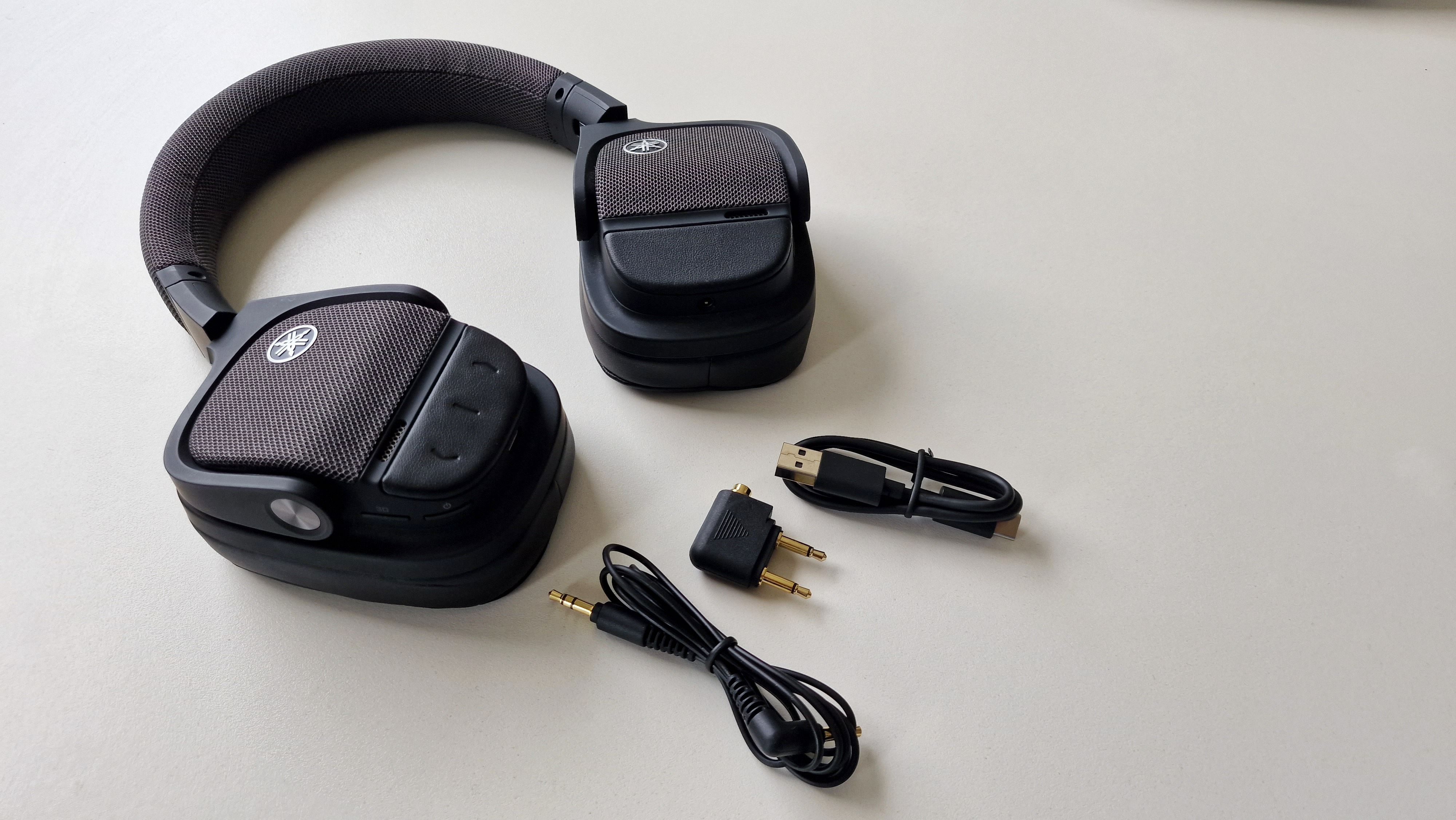 Yamaha YH-L700A ligger med av-kabel, USB-C-kabel og flyadapter på et bord.