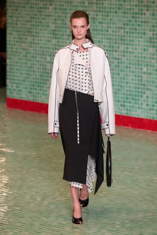 An S/S 25 model wearing a polka dot dress underneath a black skirt at the Tory Burch show.