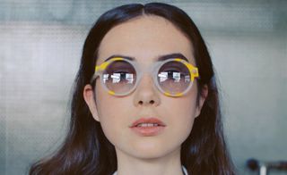 Light grey and yellow framed glasses worn by female model