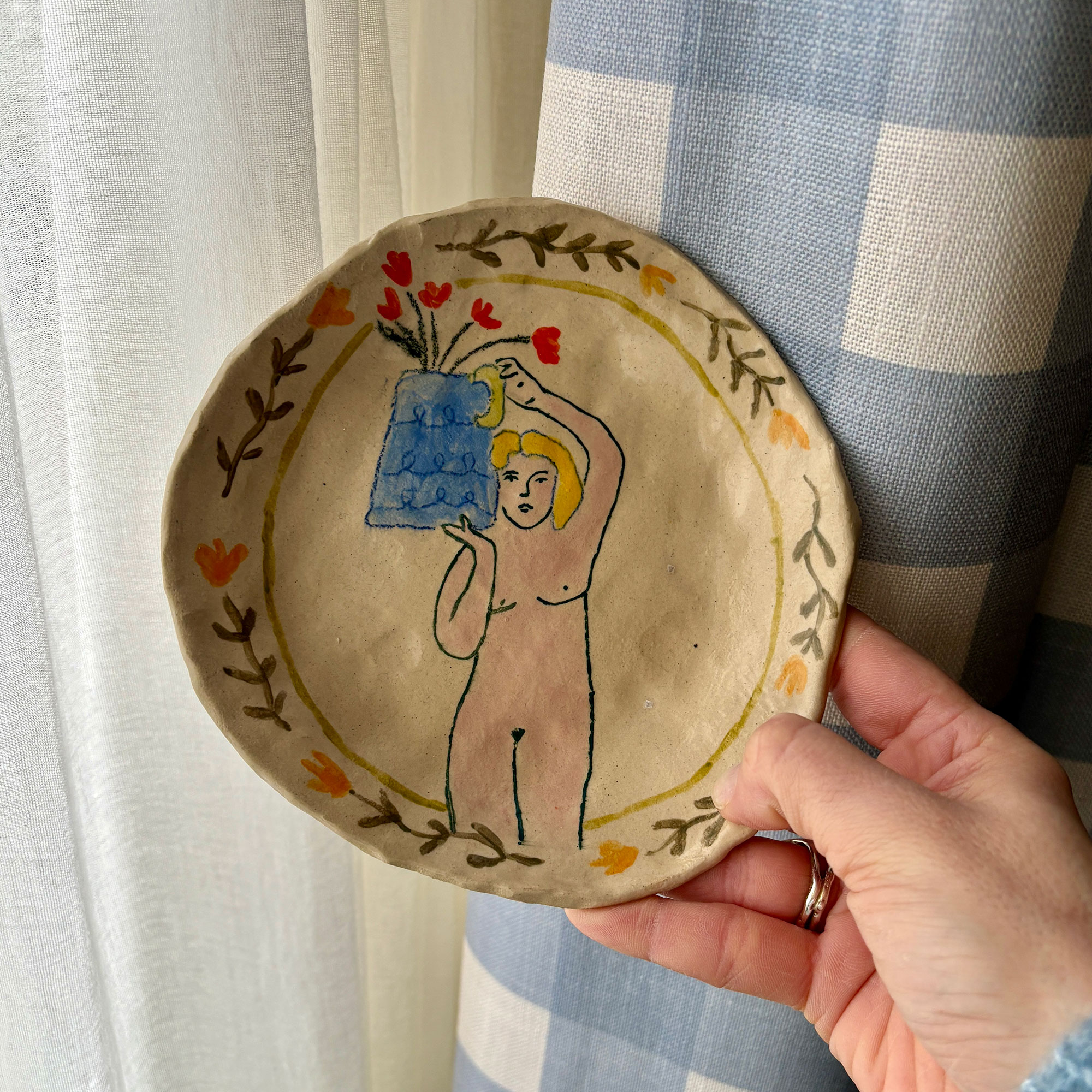 Hand holding ceramic plate painted with woman and flowers