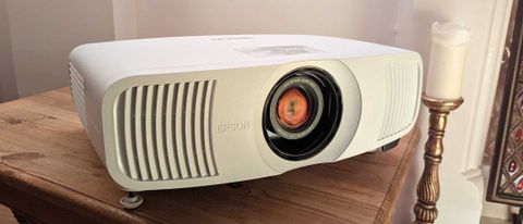 The Epson EH-LS11000W projector on a wooden table in front of a white wall