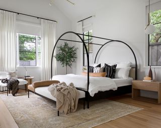White bedroom with black metal four-poster bed, white curtains and sisal rug