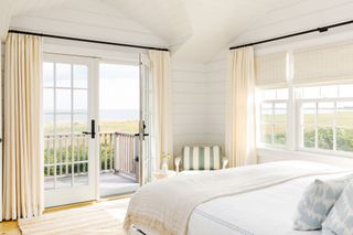 primary bedroom in beach house with French door to outdoor deck and sea views and textiles in pale blue and pale yellow
