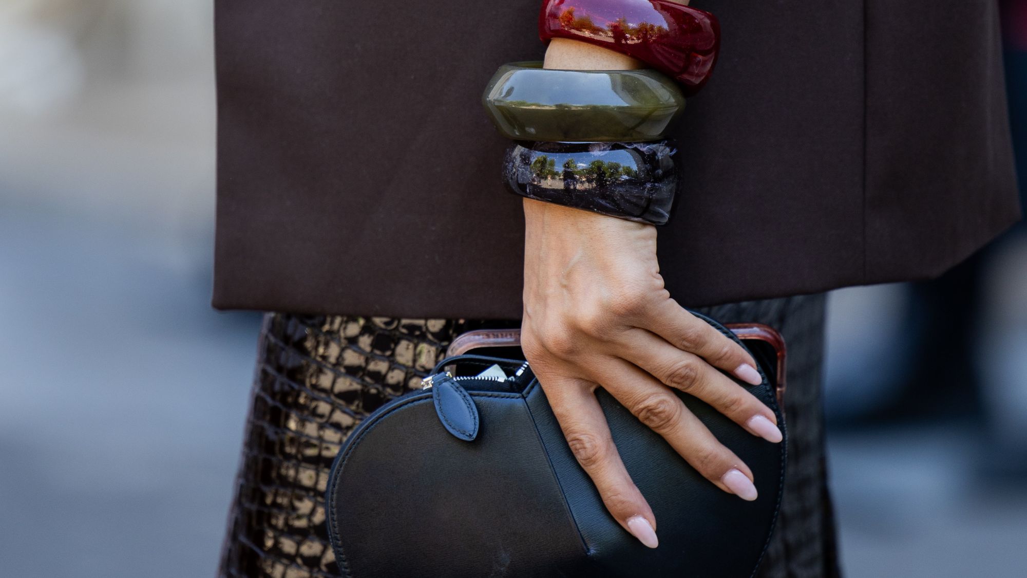 Woman holding a clutch bag, wearing three large bangles with soft serve nails