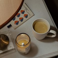 A woman reading a magazine; a flatlay of a candle, cup of tea, and book; a woman looking at a chalet in the snow