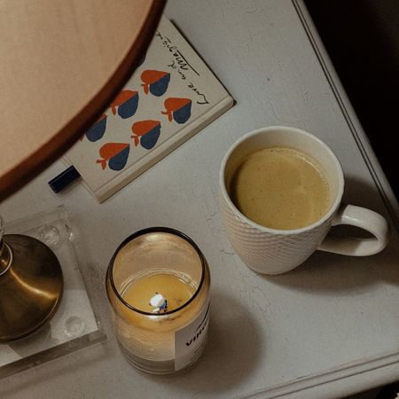 A woman reading a magazine; a flatlay of a candle, cup of tea, and book; a woman looking at a chalet in the snow
