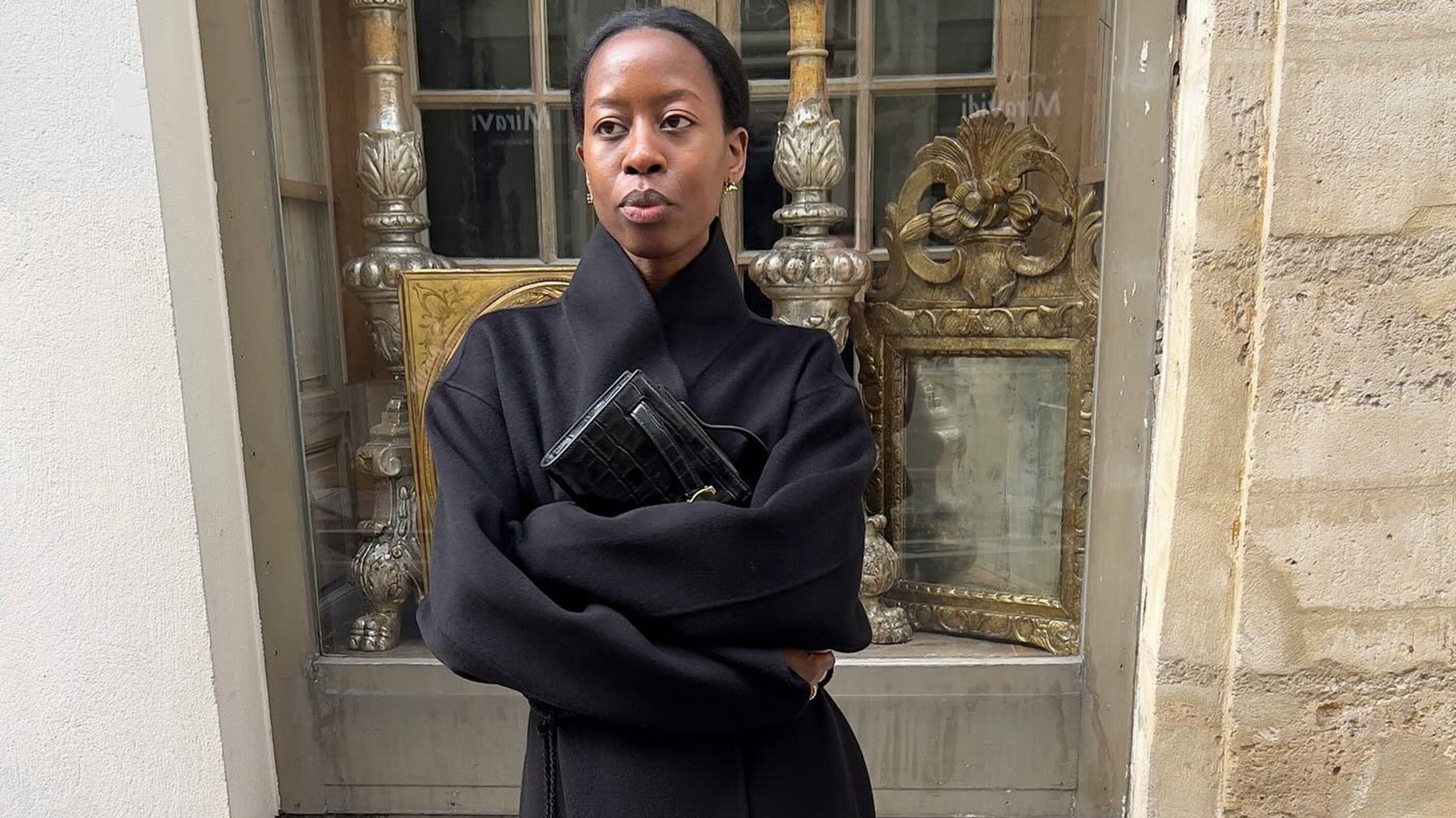 Sylvie wears a black wool coat and a clutch.
