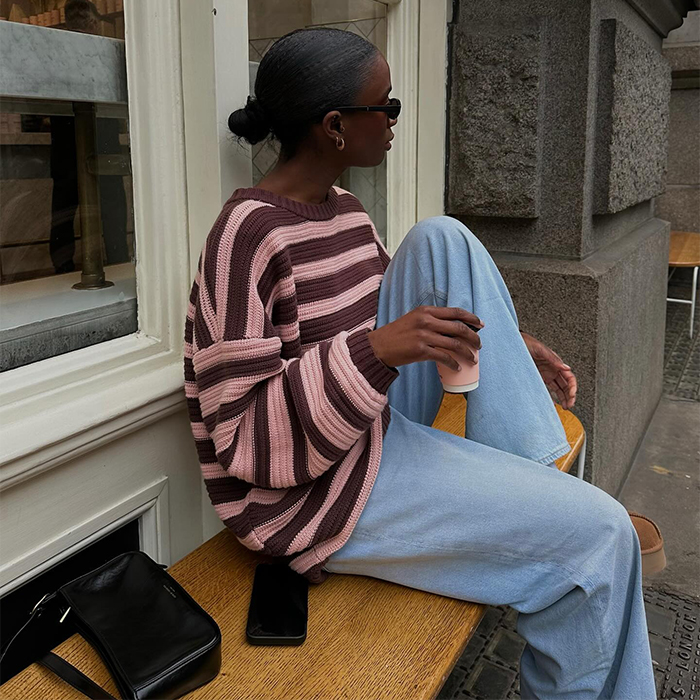 Liv wears pink and brown striped sweater and a t-while sitting on a bench