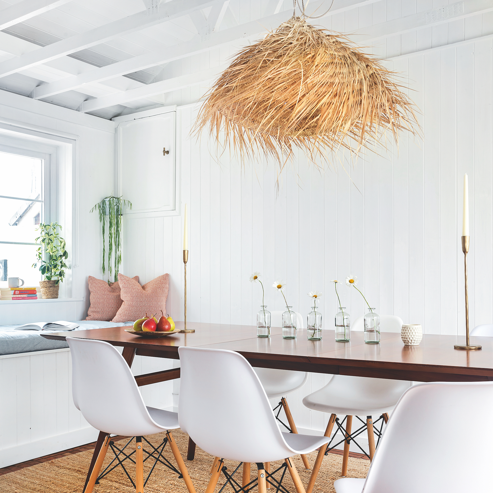 dining room with exposed rafters and wood panel walls painted white, with wooden table, white dining chairs and large grass pendant shade above table