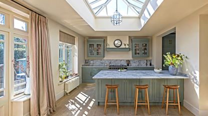 green kitchen cabinetry with sink peninsula and marble worktops