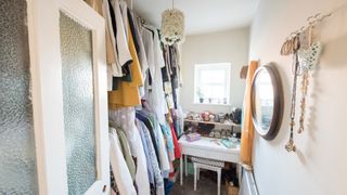 a wardrobe room with a desk and clothes hanging on rails with lots of clutter