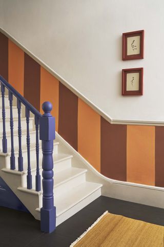 staircase with orange and red striped panelling , white steps and walls, and blue rail and spindles