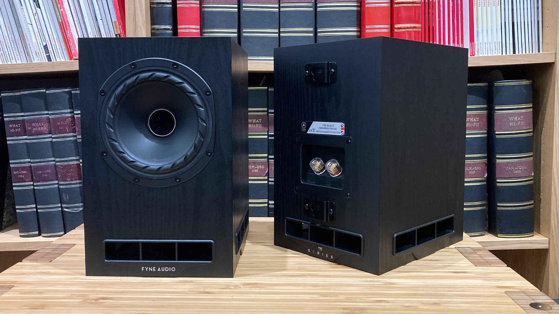 Fyne Audio F5E standmount speakers on wooden hi-fi rack in front of bookcase