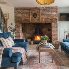 brick fireplace with log burner and velvet sofas in cottage living room