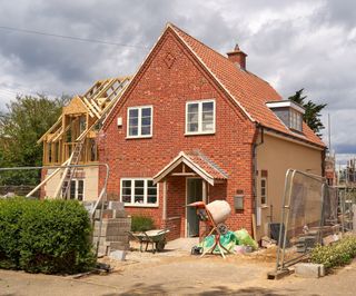 A red brick house with an extension being built to the side and timber roof trusses exposed