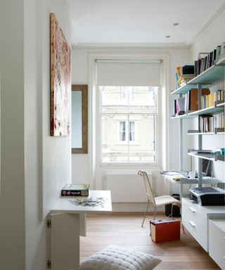 A narrow white home office with a large window in the background a chair and a desk to the right hand side, and a desk with a puzzle on it to the left