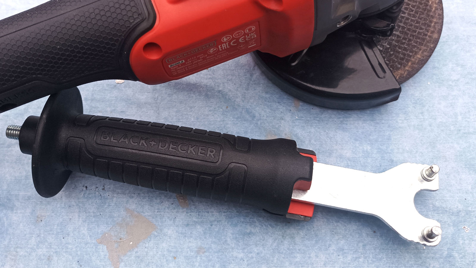 Side handle of Black + Decker angle grinder with half of two-pin spanner showing on blude dust sheet