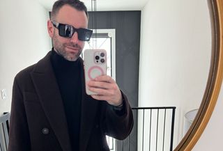 A man wearing black sunglasses and a black Vince coat over a black Vince sweater.