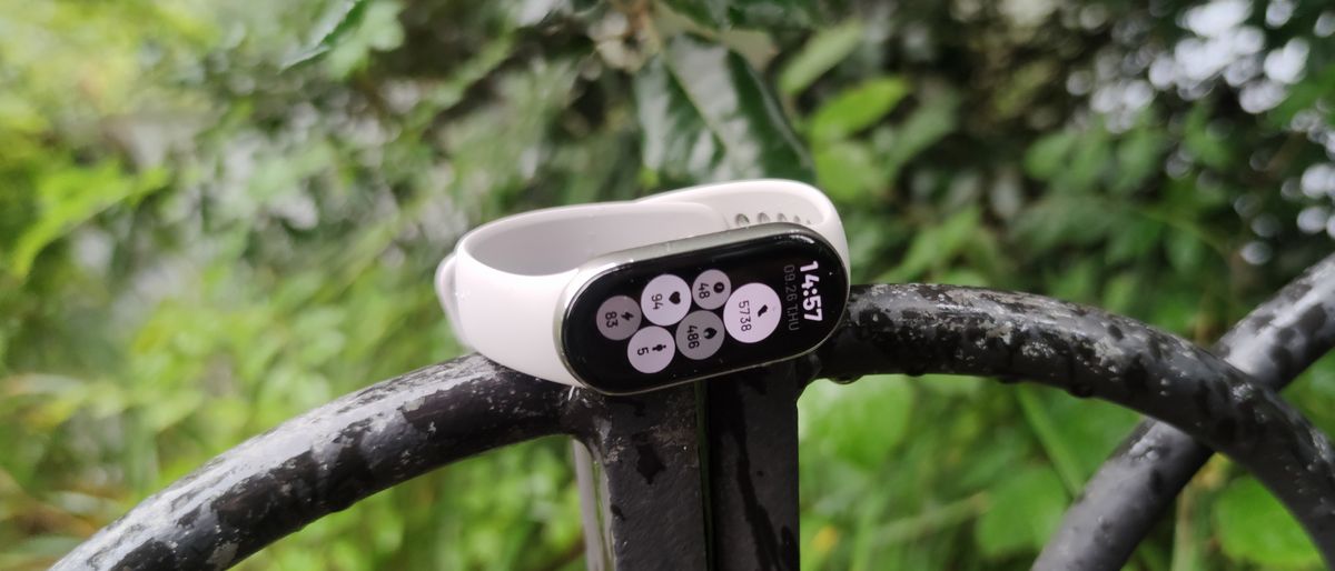 The Xiaomi Smart Band 9 on a man&#039;s wrist in front of a green park.